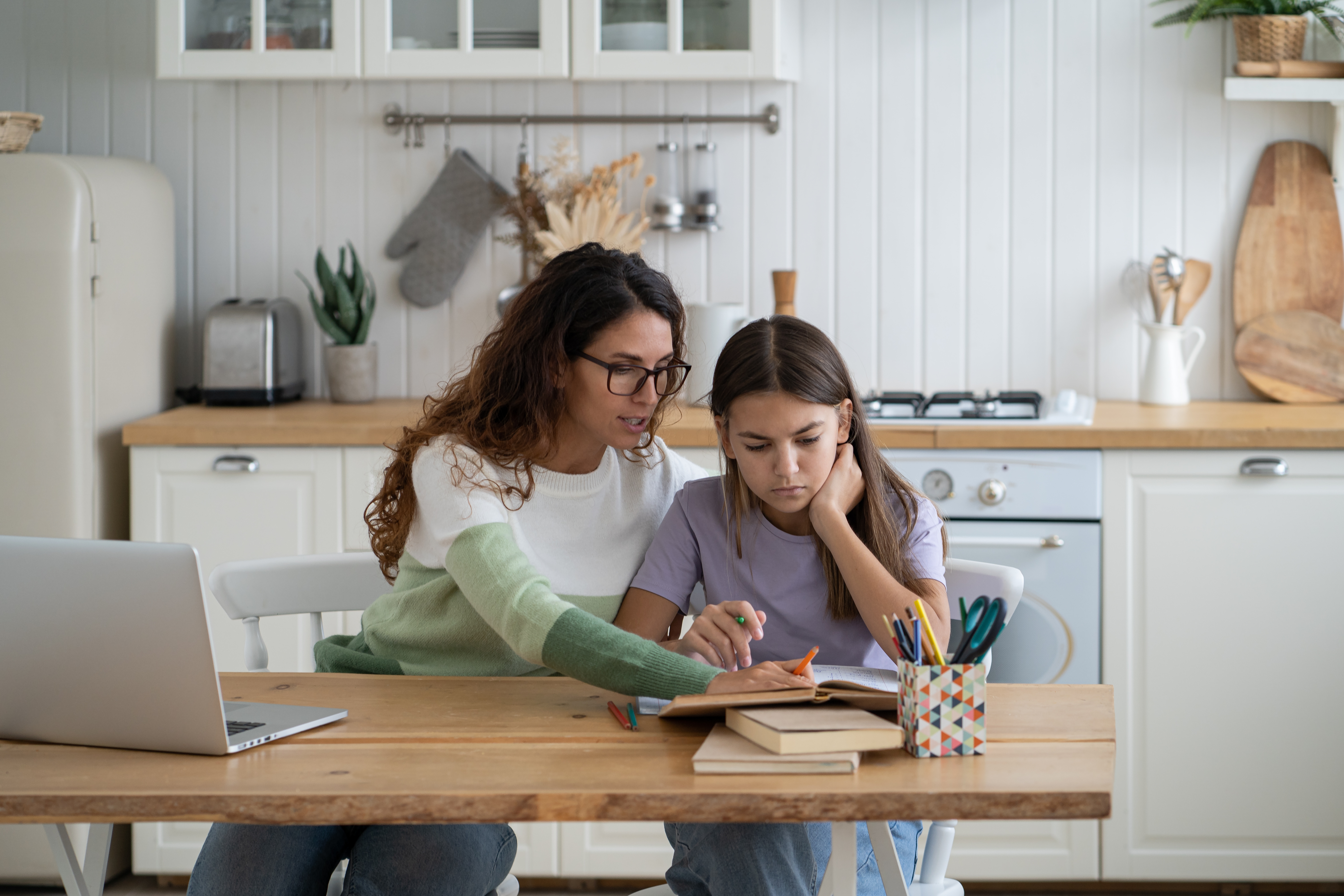 Mother guiding daughter with schoolwork at kitchen table