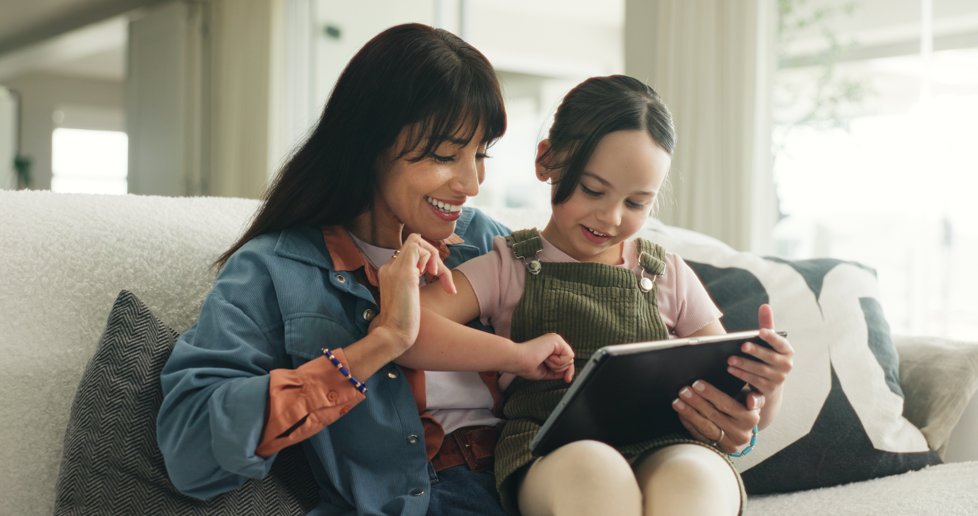 Mother and daughter exploring a tablet together on the sofa
